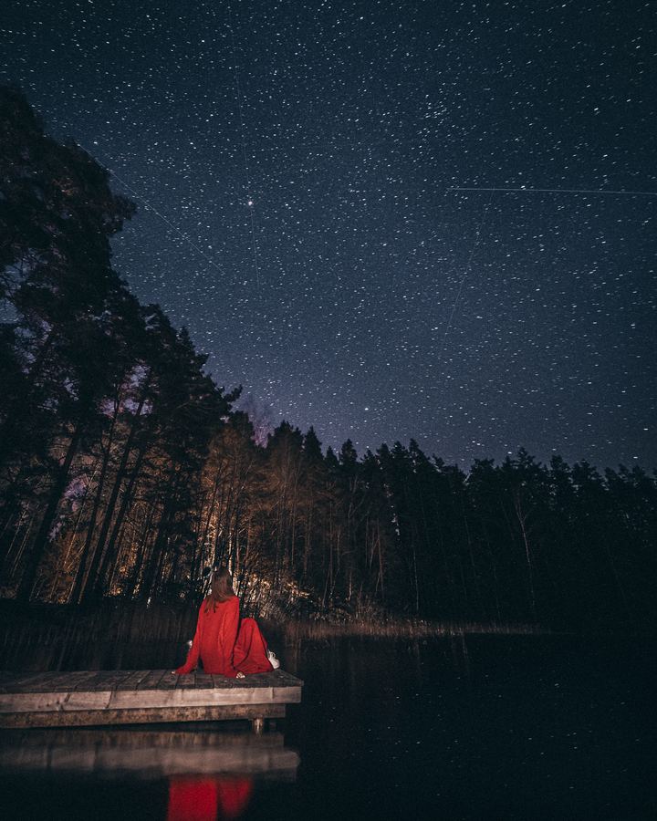 Someone in red sitting on the pier under a sky full of stars