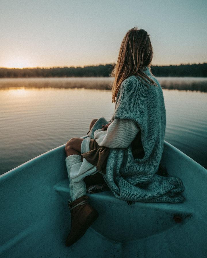 Someone wrapped in a blanket in a boat on the misty morning lake